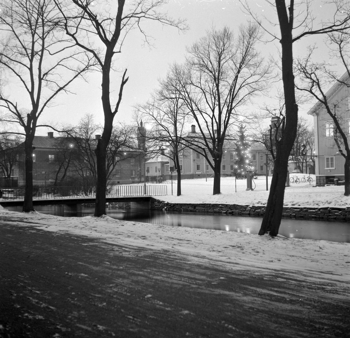 Fotografiet taget över Lillån mot Östra torgbron, Stora torget och Rådhuset. Snö ligger på marken. 1940/50