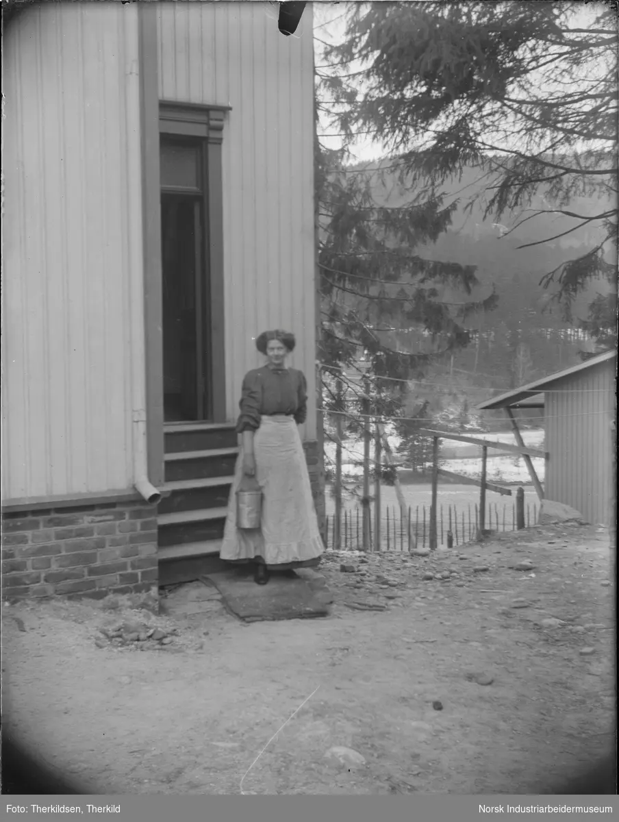 Kvinne med spann i hånden stående utenfor Solvang, senere kalt Hellandgården.
