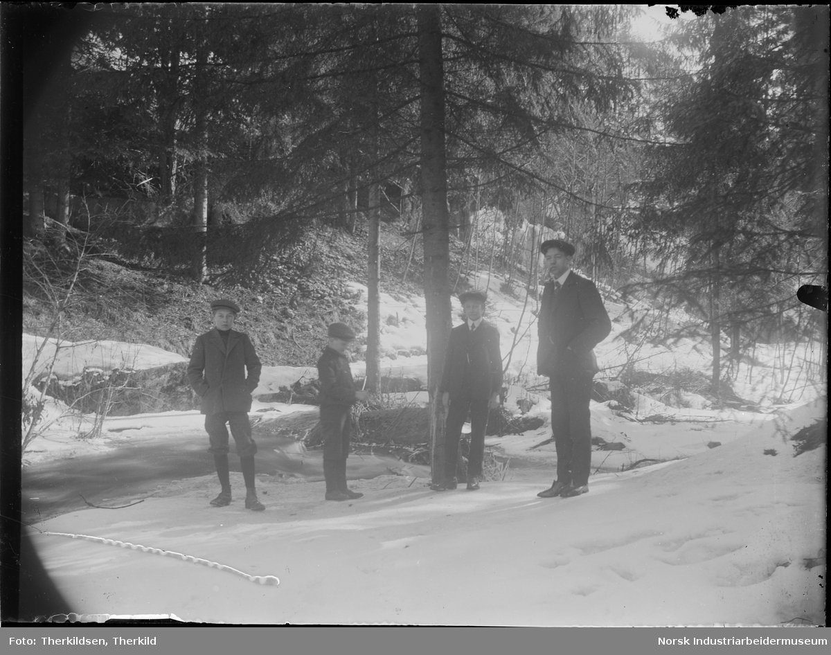 En mann og tre gutter med sixpence stående i skogsterreng.