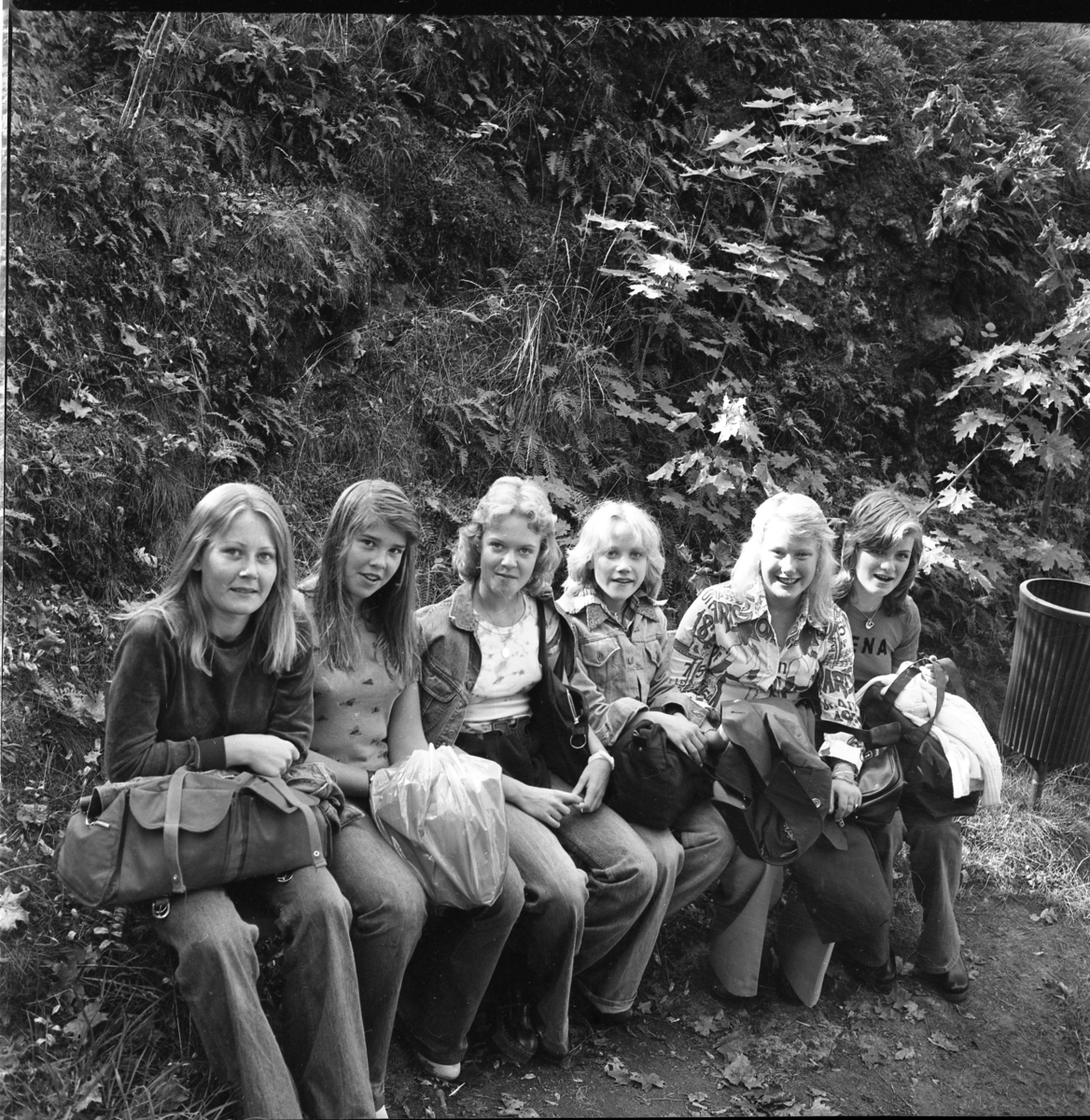 Sex flickor sitter på en bänk i en parkmiljö.