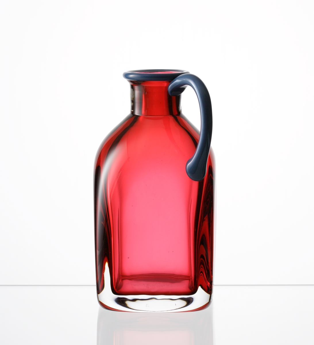 Formgiven av Erika Lagerbielke. Fyrkantig flaska "Confetti" i rosa underfång, med blå mynning och hänkel.