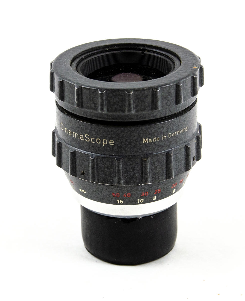 Objektiv till CinemaScope-projektor, typ Möller-Anamorphot 32/2x. Förvarad i ett anpassat läderfodral. På fodralet står det med svart tuschpenna: "CinemaScope-objektiv FM-Foto Flygvapenmuséet Malmen". Objektivet är tillverkat i Tyskland.