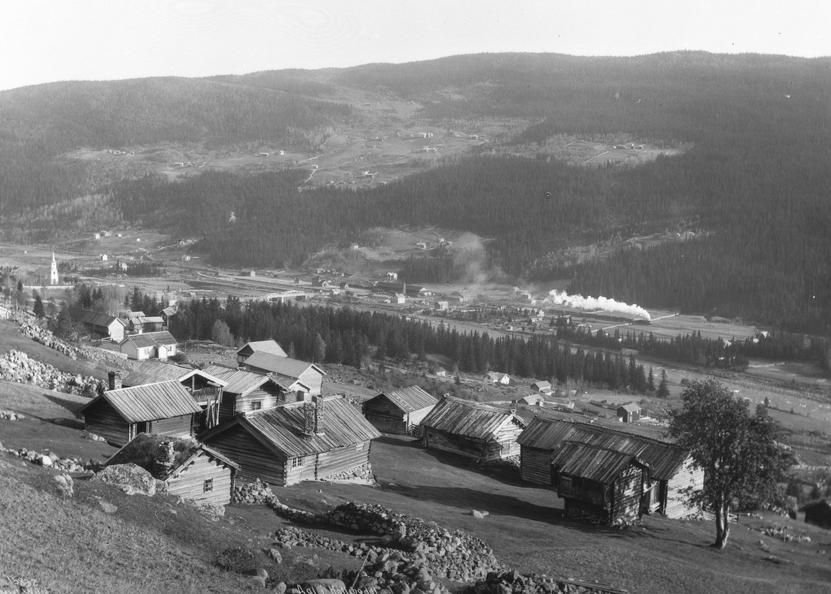 Utsikt over Ål i Hallingdal med damptog på vei gjennom landskapet og en samling laftede bygninger i forgrunnen, 5. oktober 1913.