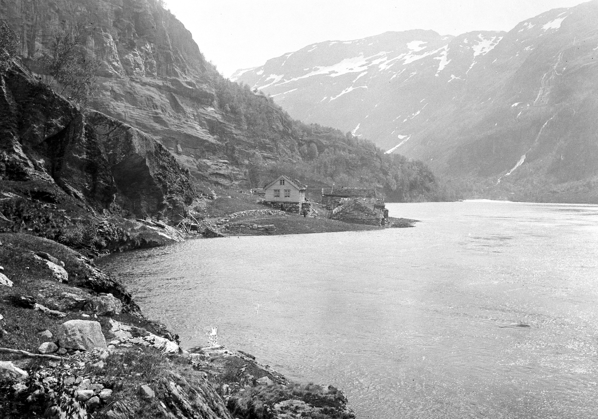 Lite gårdsbruk med bygnignsmasse til dels i stein ved vannkanten under bratte fjell på Nesbø ved Nesbøvatnet i Aurlandsdalen, 1914.