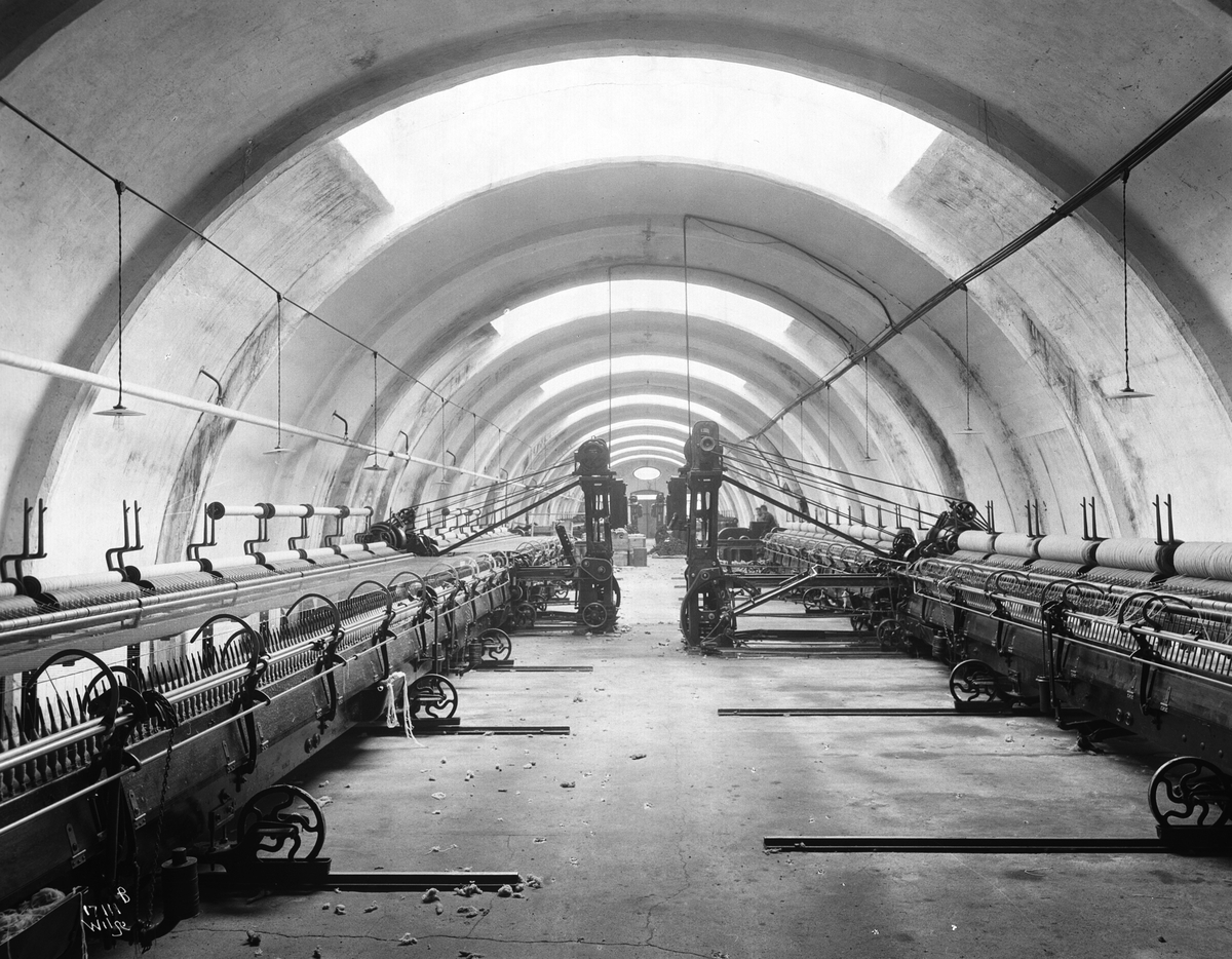 Mange vevmaskiner står i to rader i en hall, Heggdal Ullvarefabrikk. Fotografert 1923.