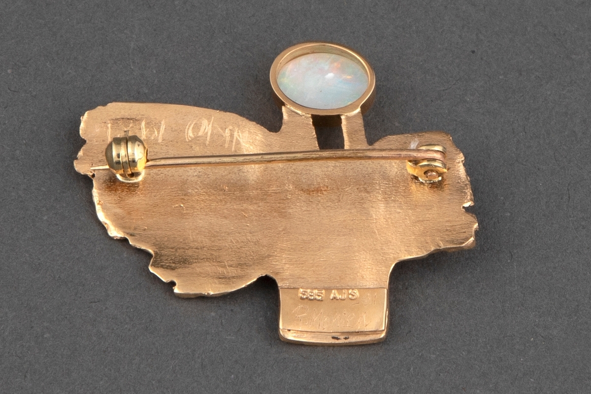 Brosje av gull i slyngestøpsteknikk med hvit opal. Brosjen har en uregelmessig form som minner om en fugl med vinger, stjert og hode. Overflaten er ujevn. Opalen er satt inn i en blank innfatning. Baksiden er glatt og har nål.