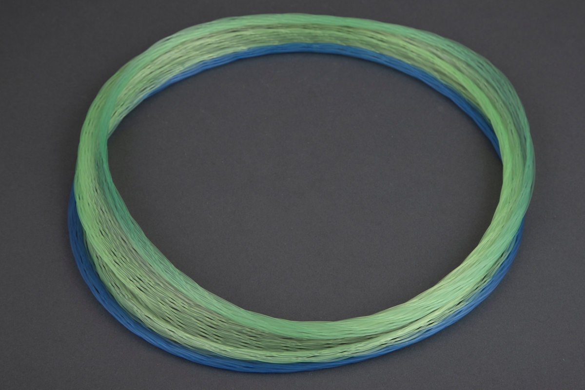 Halsring av nylontråd. Blå, gule og grønne tråder er flettet slik at de danner en elastisk ring som kan trekkes ut til forskjellige former.