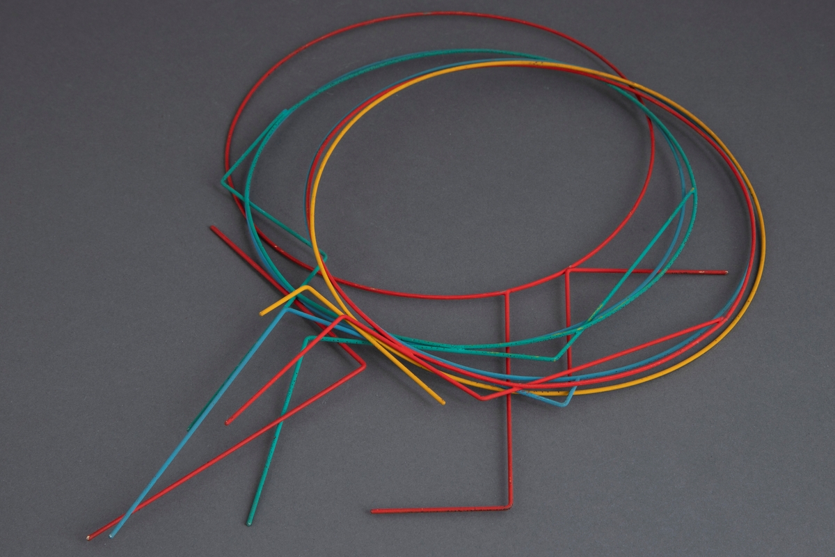 Halssmykke bestående av seks separate ringer av stål som hver har en påloddet dekorasjon sammensatt av rette tråder av stål. Alt er dekket av neopren i ulike farger. To ringer er røde, to blå, en gul og en grønn.