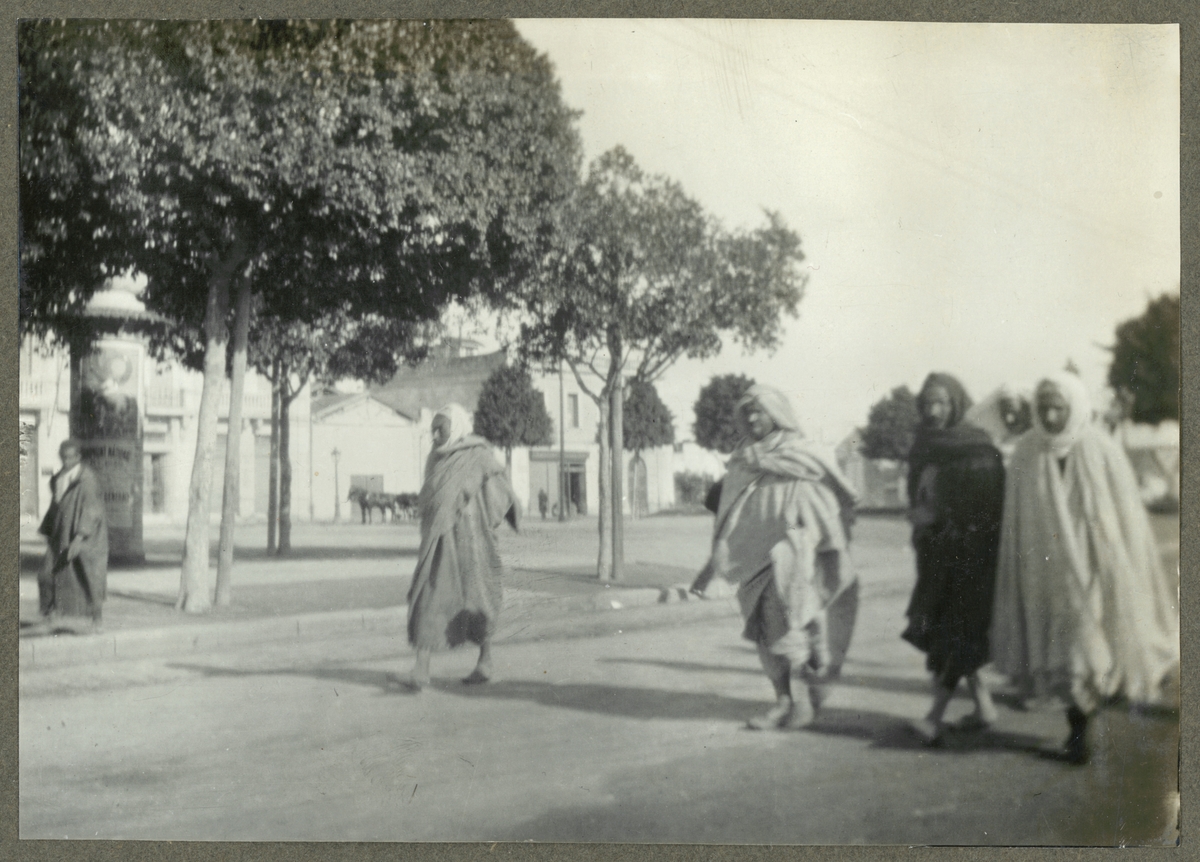 Bilden visar människor i arabiska kläder gåendes på en gata i Alger.