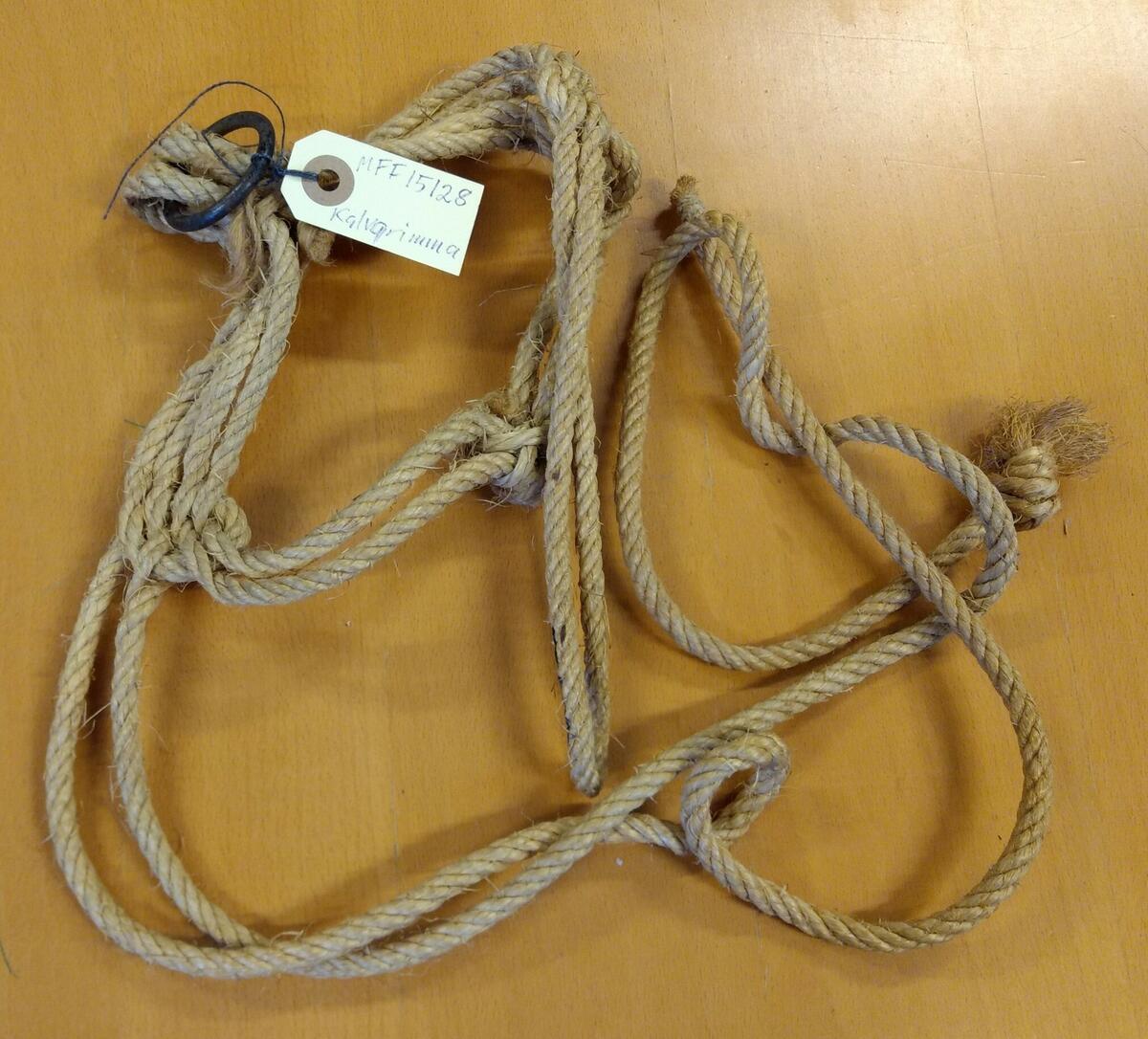 Kalvgrimma av jute. Övre delen består av dubbla rep. Underdelen består av 4-dubbla rep. Stålring under hakan. Två rep att knyta runt nacken. Givare: Harry Sjöström.