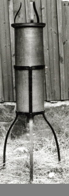 a) Trefotsstativ av järn. Svartfärgat. Upptill format för att passa en cylinder. Höjd 45,5 cm.b) Cylinder av keramik. Med avtappningsstrut i bottnen. Upptill en mjukt avrundad krage. Struten försedd med glasrör och gummislang med klämma. Höjd 77 cm, diameter 21 cm.c) Järnhätta med centrumhål. På hättan står tre S-formade elastiska hållare i järn.d) Platta av keramik. Perforerad. Stort centrumhål med krage. Diameter 19 cm, tjocklek 1 cm. 3 cm hög.e) Platta (sprucken) lika som d).