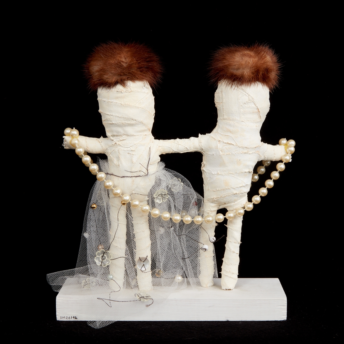 Friskulptur "I vinter blir det kallt" av Anna Sjons Nilsson. En manlig och en kvinnlig figur av vit gipsbinda. Figurerna har bruna pälsbitar på huvudet, knappar till ögon och är klädda i tyll, reflexbricka och pärlor. Sockel av trä.