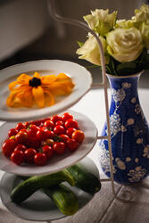 Foto av etasjefat med tomater og agurker. Vase med roser. Nærbilde.