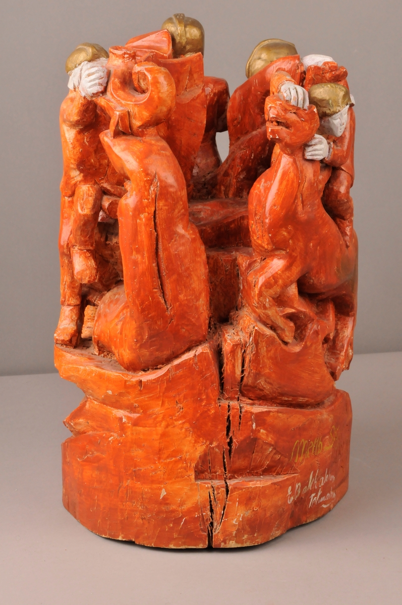 Skulptur av 4 riddere rundt ein kubbe og 4 dyrefigurer. Raud farge, ridderene har bronsefargede hjelmer, kvite ansikt og hender. Nede på foten av skulpturen er det innskripsjon.