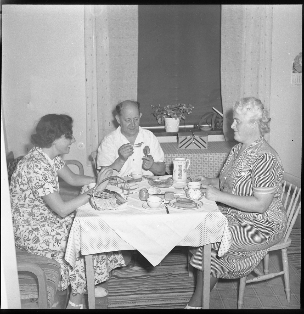 Kerstin Åsén tillsammans med okänd man och kvinna vid ett köksbord, aug 1950.