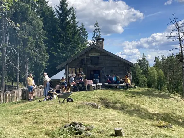 Sommer på Skålbergsætra. Mennesker koser seg i sola utenfor seterbygget.