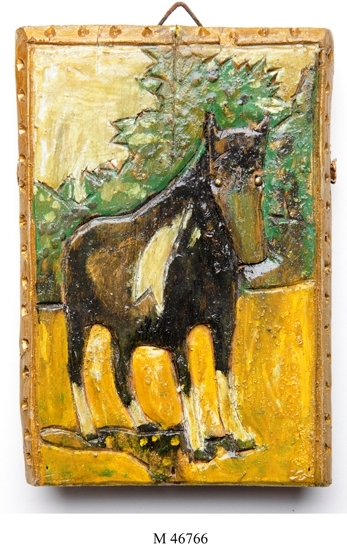Trärelief. 
Platt utskuren trärelief. Målad i grönt, gulvitt och svart.
Föreställer en häst stående i ett landskap med gröna träd
i bakgrunden. Ramen är skuren i reliefen och guldbronserad.

Inskrivet i huvudbok 1985.
Montering/Ram: Ej ramad