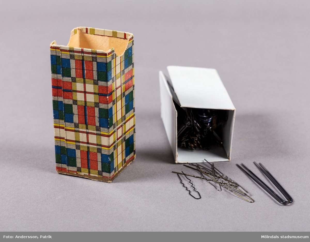 En liten rektangulär ask som innehåller hårnålar. Asken har ett lock som öppnas uppåt. Asken är dekorerad med ett geometriskt mönster som är indelat i rutor och ränder. Askens mönster liknar en Mondrian målning.