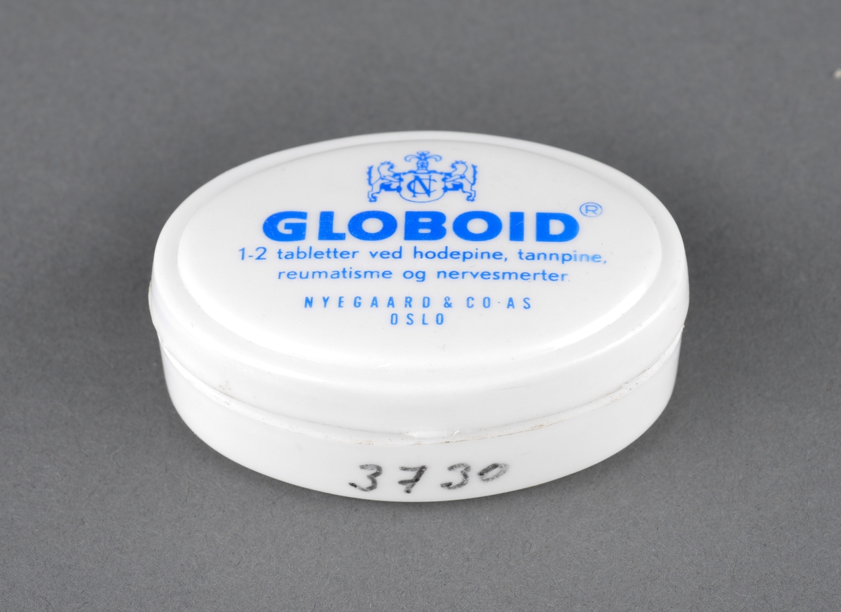 Hvit, oval plasteske for oppbevaring av smertestillende medisin. Merke: Globoid.
Gitt som gave til museet av tidligere kjøpmann Rolf Kaald.