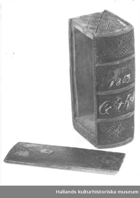 Bokfodral i form av en bok. Asken är snidad i ett stycke och har skjutlock som löper i en fals. Asken är dekorerad med romboidiska mönsterfält i ristningsteknik och med uddsnittsbårder. Asken är bemålad senare eller ommålad i grönt med ryggfalsar i rött och fläckar av blått. På ryggen är ristat "BTS" och målat "1863 CAAS". 