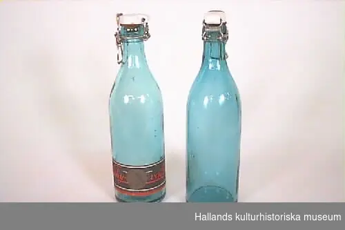 a) Flätad korg av säv. Längd: 33 cm, bredd: 25 cm, höjd: 16 cm.Rektangulär med handtag och sex fack, 10 x 11 cm. b-c) Flaska, glas, grön. Etikett saknas. Höjd: 23 cm, diameter: 7 cm.Patentkork av porslin. d) Flaska, glas, grön.Höjd: 23 cm, diameter: 7 cm. Patentkork av porslin. Rektangulär etikett, rosa botten, svart text: "APOTEKARNES VATTENFABRIK - BITTERVATTEN". Även etikett runt halsen. e) Flaska, glas, grön. Höjd: 23 cm, diameter: 7 cm. Patentkork av porslin. Etikett: Vit botten, röd och svart text: "KLIPPANS VICHYVATTEN." (Se etikettens form på scannad bild.) f) Flaska, glas, ljusgrön. Höjd: 23 cm, diameter: 7 cm.Patentkork av porslin. Trasig rektangulär etikett, gul botten, svart text:  "- VATTEN, AKTIEBOLAGET NYA BRYGGERIET I BORÅS.""g) Flaska.Höjd: 24 cm, diameter: 7 cm. Etikett saknas. Av glas. Ljusgrön. Patentkork av porslin. h) Flaska. Höjd: 24 cm, diameter: 7 cm. Av glas. Ljusgrön. Patentkork av porslin. Rektangulär etikett, gul botten med svart text: "Bryggeriaktiebolaget FALKEN, Vichyvatten." i-j) Flaska. Höjd: 24 cm, diameter: 7 cm. Av glas. Ljusgrön. Patentkork av porslin. Rektangulär etikett, svart botten med guld. Röd text: "Vichyvatten, Bryggeriaktiebolaget FALKEN, Falkenberg."