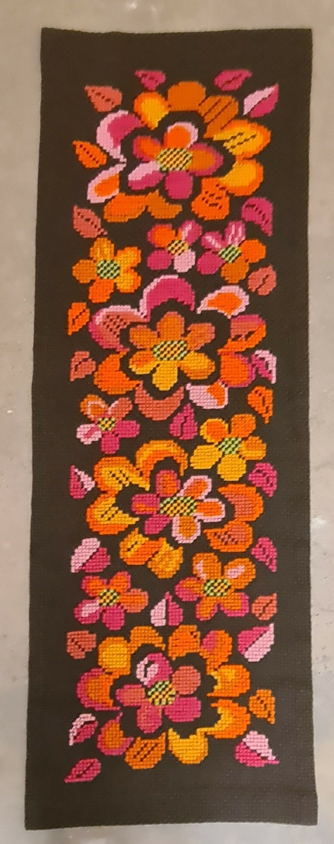 Brun vepa av grov aidaväv, broderad i korsstygn med ullgarn (Sudangarn) i korsstygnsbroderi, blommor i rosa, gult och orange.