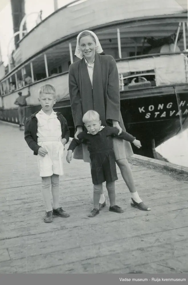 På kaia i Vadsø på 60-tallet. Gerd Arnesen og tantebarna Erling Jan og Alf Harald Olsen. Hurtigruta Kong Haakon ligger ved Dampskipskaia.