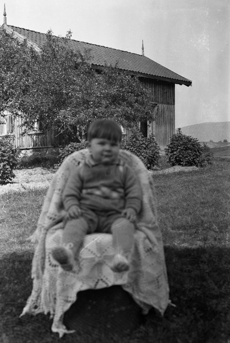 Portrettfoto av barn i stol framfor hus.