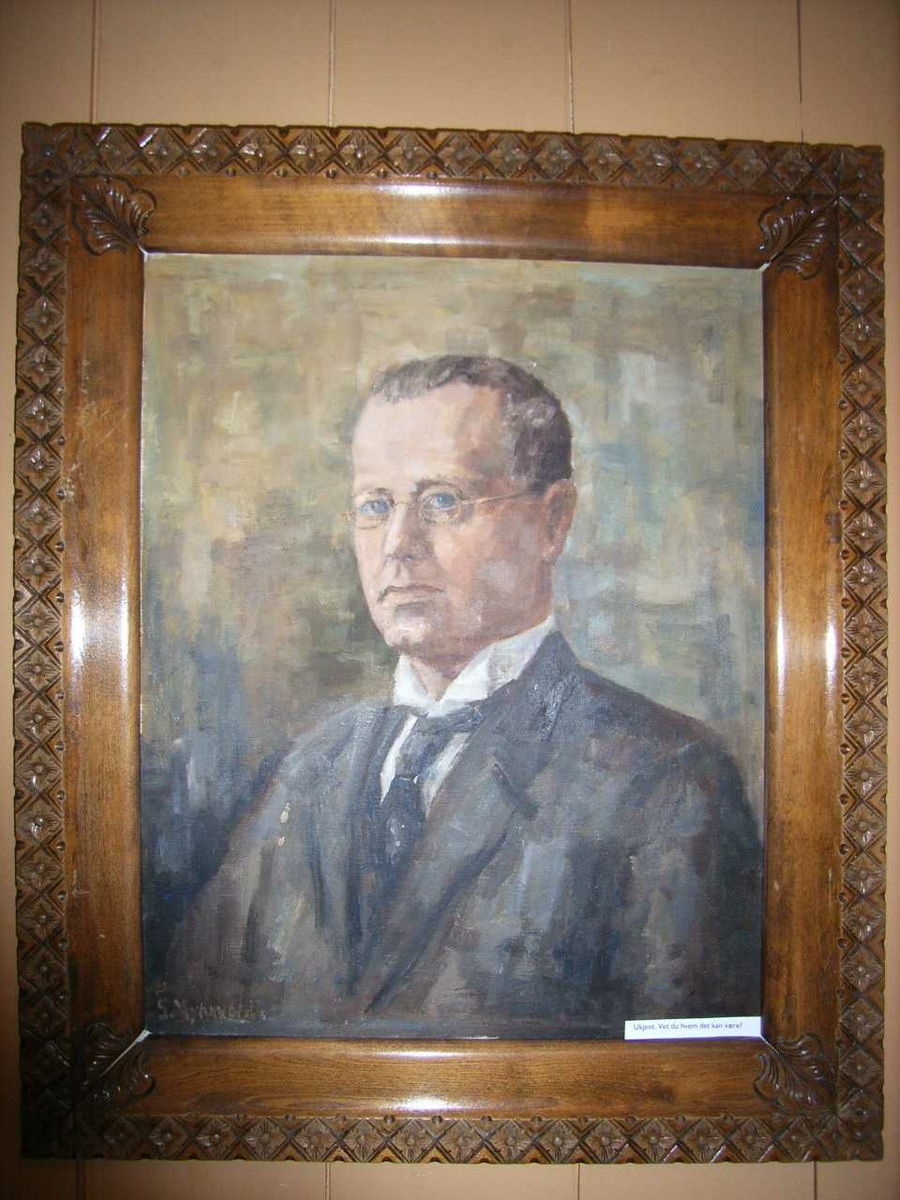 Portrett av ung mann. Ikledd hvit skjorte, sort slips og sort jakke, med briller