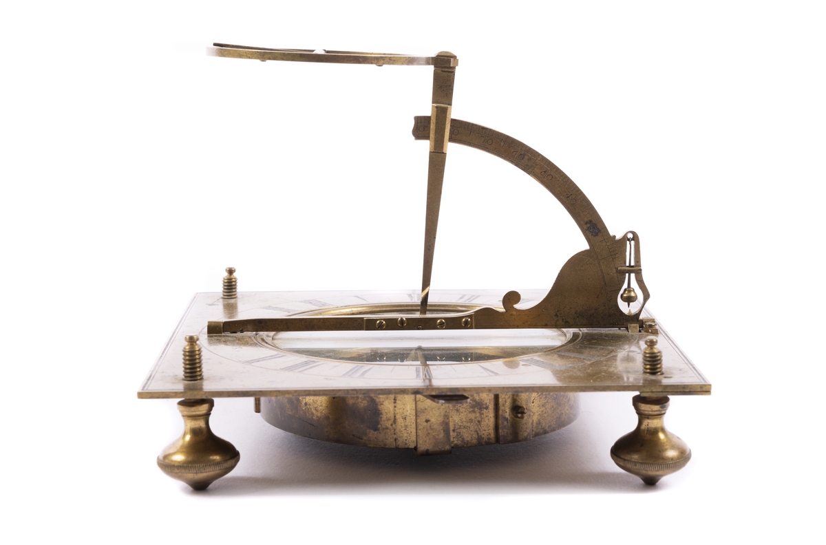 Solur med ställbar latitudbåge med skuggpinne och timcirkel samt ett mindre upphängt lod. Stativets platta har fyra skruvfötter. Ring angivande timmar graverade runt en glastäckt kompass.
Tillverkare Westber, Carl Hindric, 1720-1769