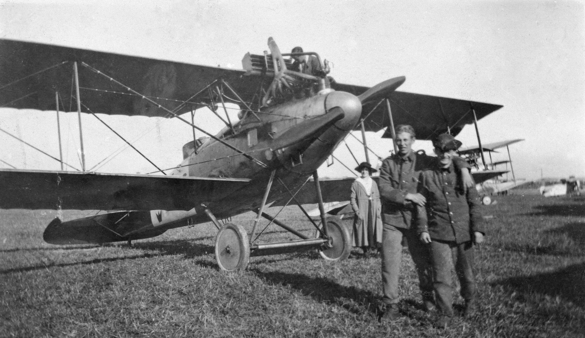 Tre militärer och en kvinna vid flygplan FVM S 18 på ett fält, omkring 1919-1926.