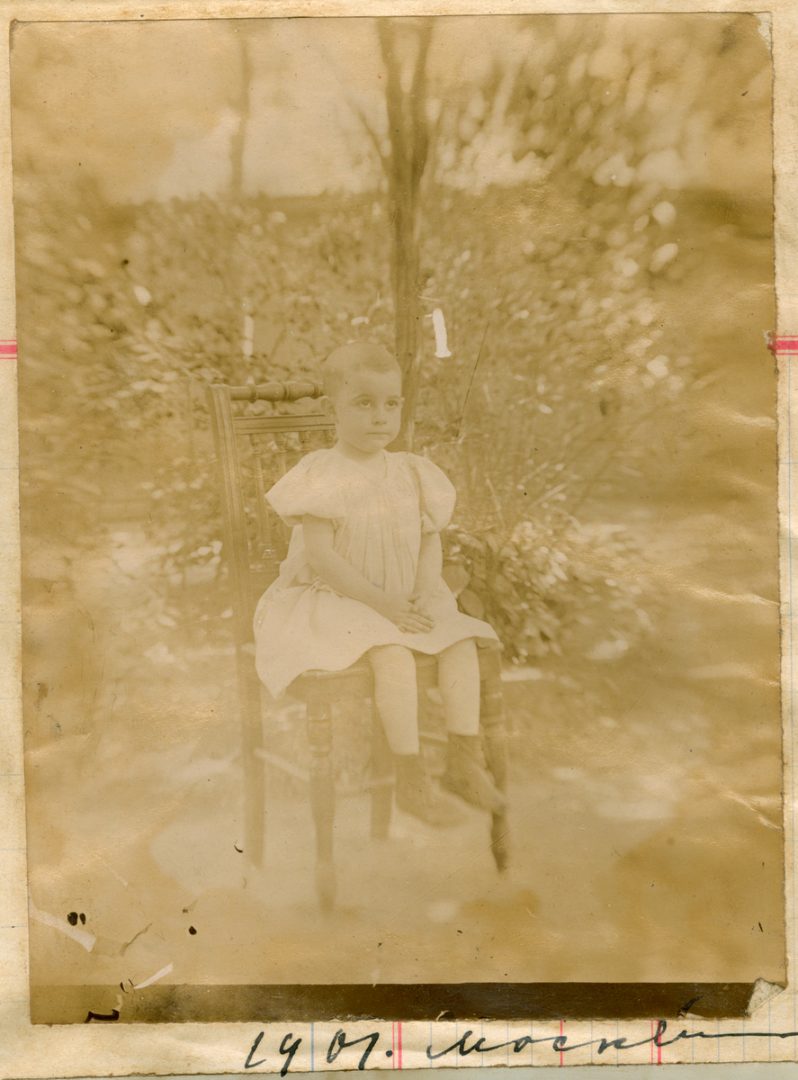 Portrett av et barn, antagelig Serafima Rostin kortklippet, sittende på en stol. Fotografert utendørs i Moskva i 1901.