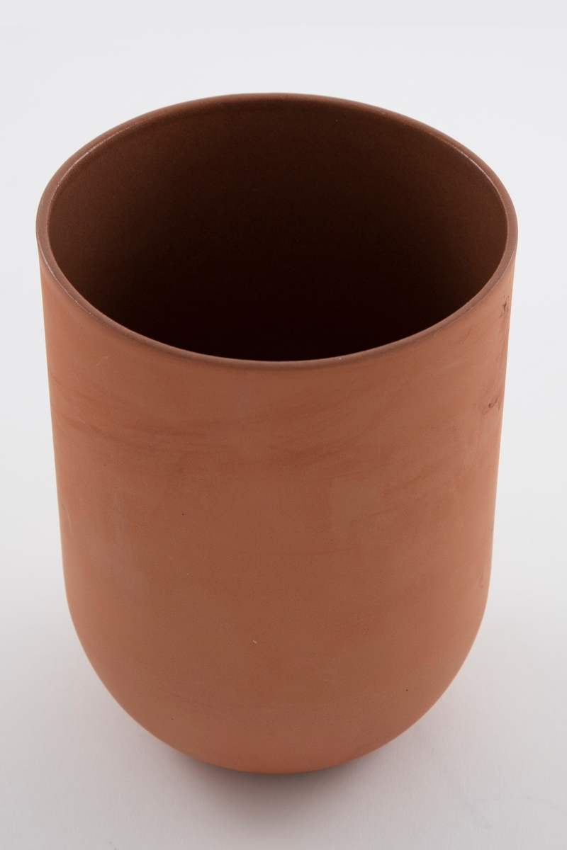 Brun vase i terrakotta. Sylinderformet korpus med bunn formet som en halvsfære. Åpen munning. Uglasert på utsiden og glasert på innsiden.