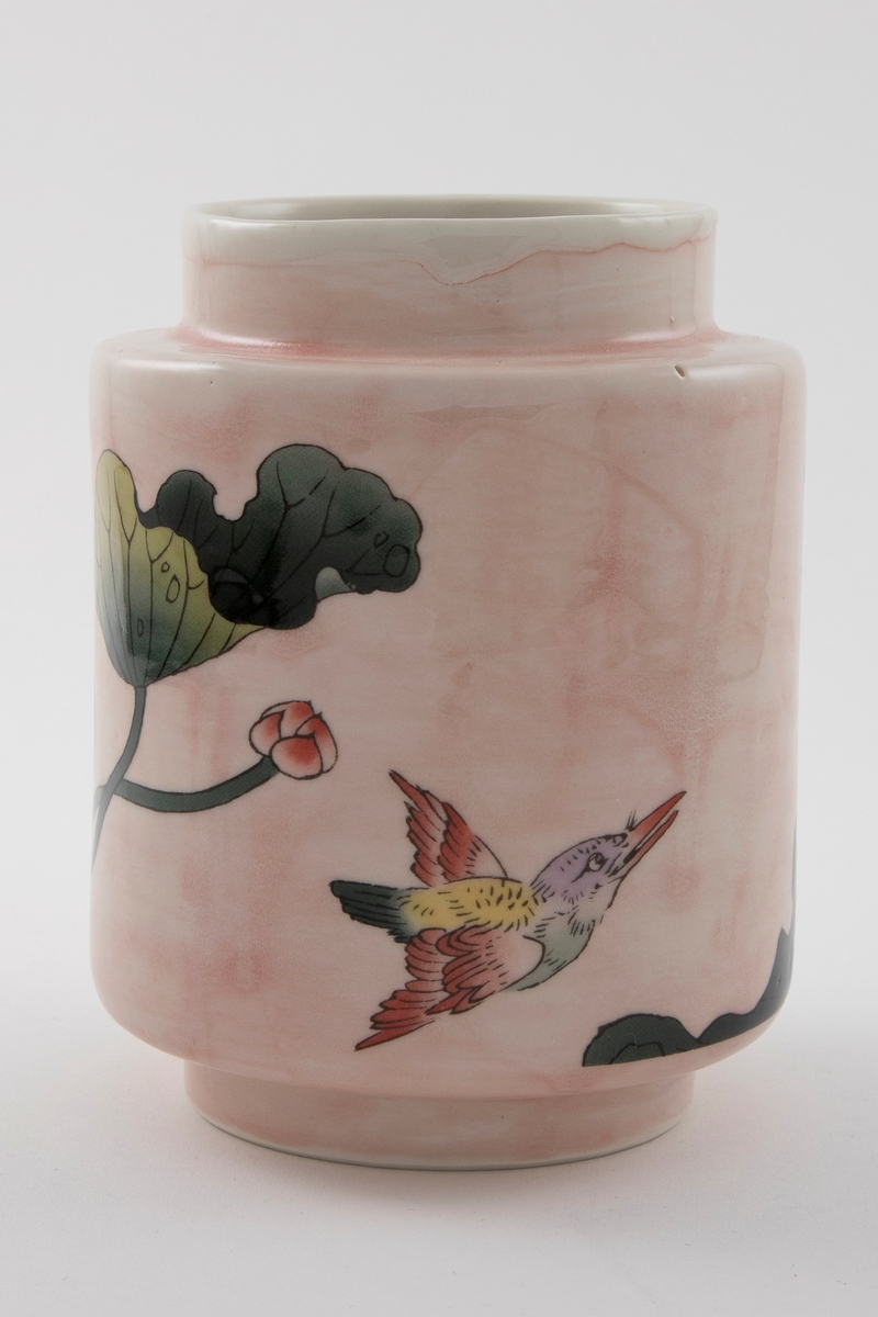 Blank sylinderformet porselensvase med halvtransparent rosa glasur. Lav fot og kort hals med åpen munning. Dekaler med blomster, blader og en fargerik fugl på vasens korpus. Blank hvit glasur på innsiden.