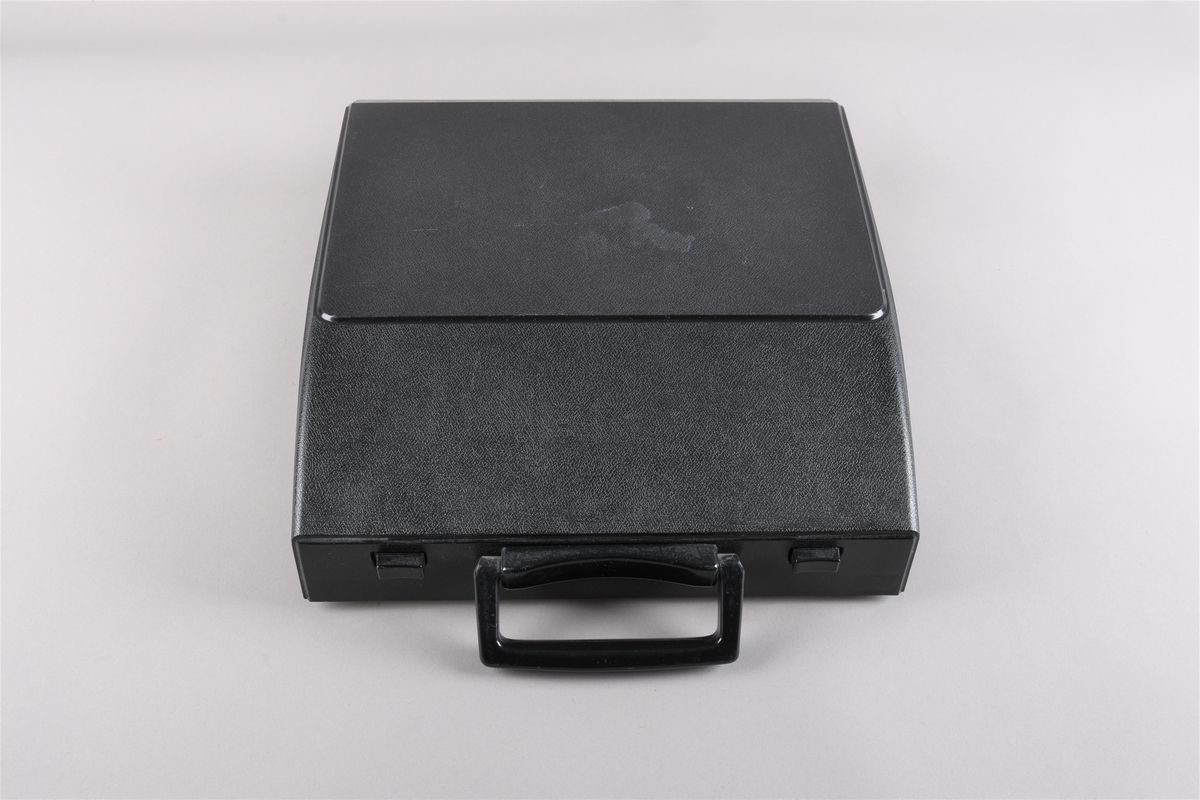 Berbar skrivemaskin/reiseskrivemaskin med koffert/deksel som klipsast på skrivemaskina når denne ikkje er i bruk. Kofferten har handtak i framkant. Skrivemaskina har querty-tastatur og fargeband i raudt og svart.