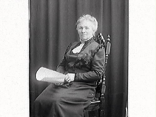 Ateljéporträtt av friherrinnan Fägersköld sittande på en stol med ett dokument i händerna.
