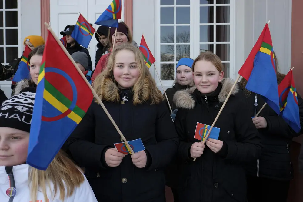 Elever står på trappa til Eidsvollsbygningen med samiske flagg i hendene.