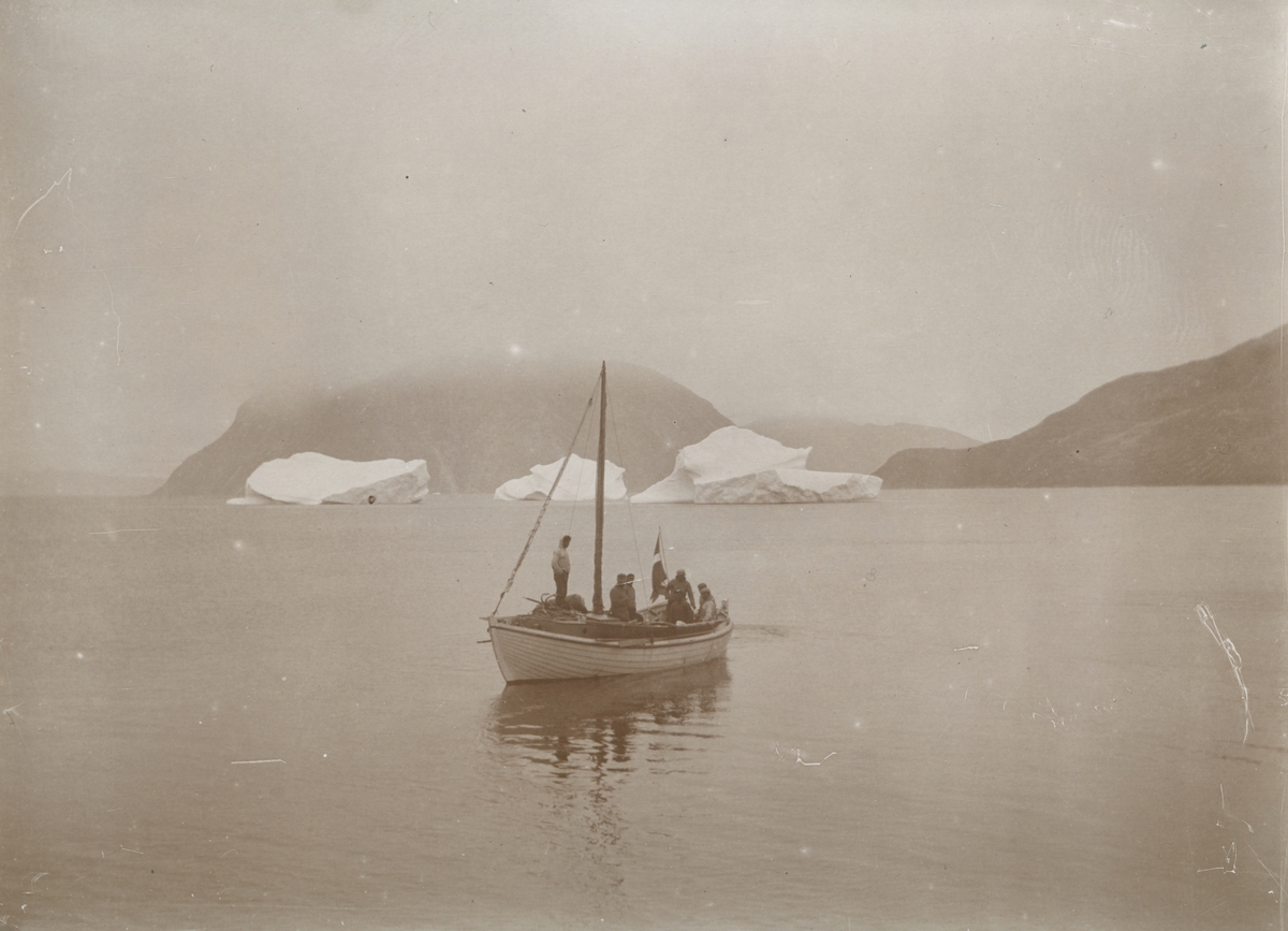 Fotografi från expedition till Grönland. Motiv av ett antal fiskare ute på havet i en fiskebåt. I bakgrunden syns tre mindre isberg.