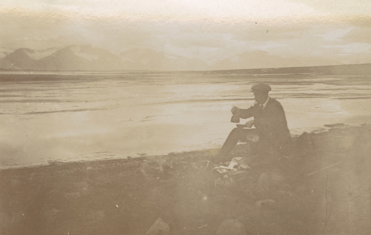 Fotografi från expedition till Spetsbergen. Motiv av man som dricker kaffe på en stenig strand vid havet.