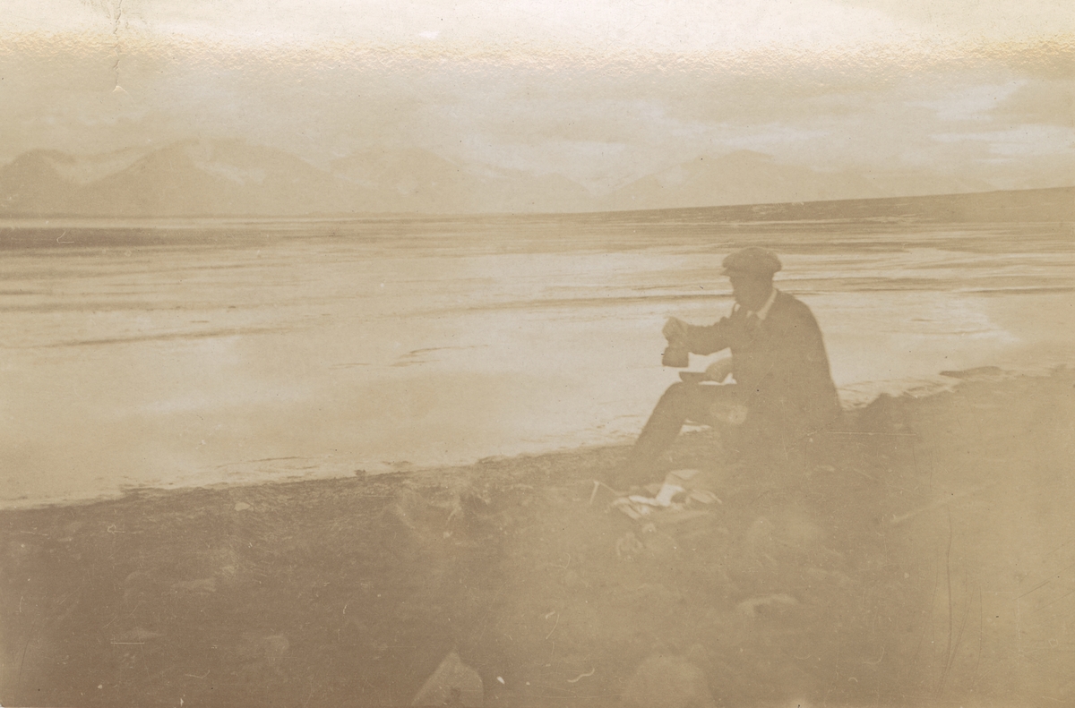 Fotografi från expedition till Spetsbergen.  Motiv av man som dricker kaffe på en stenig strand vid havet.