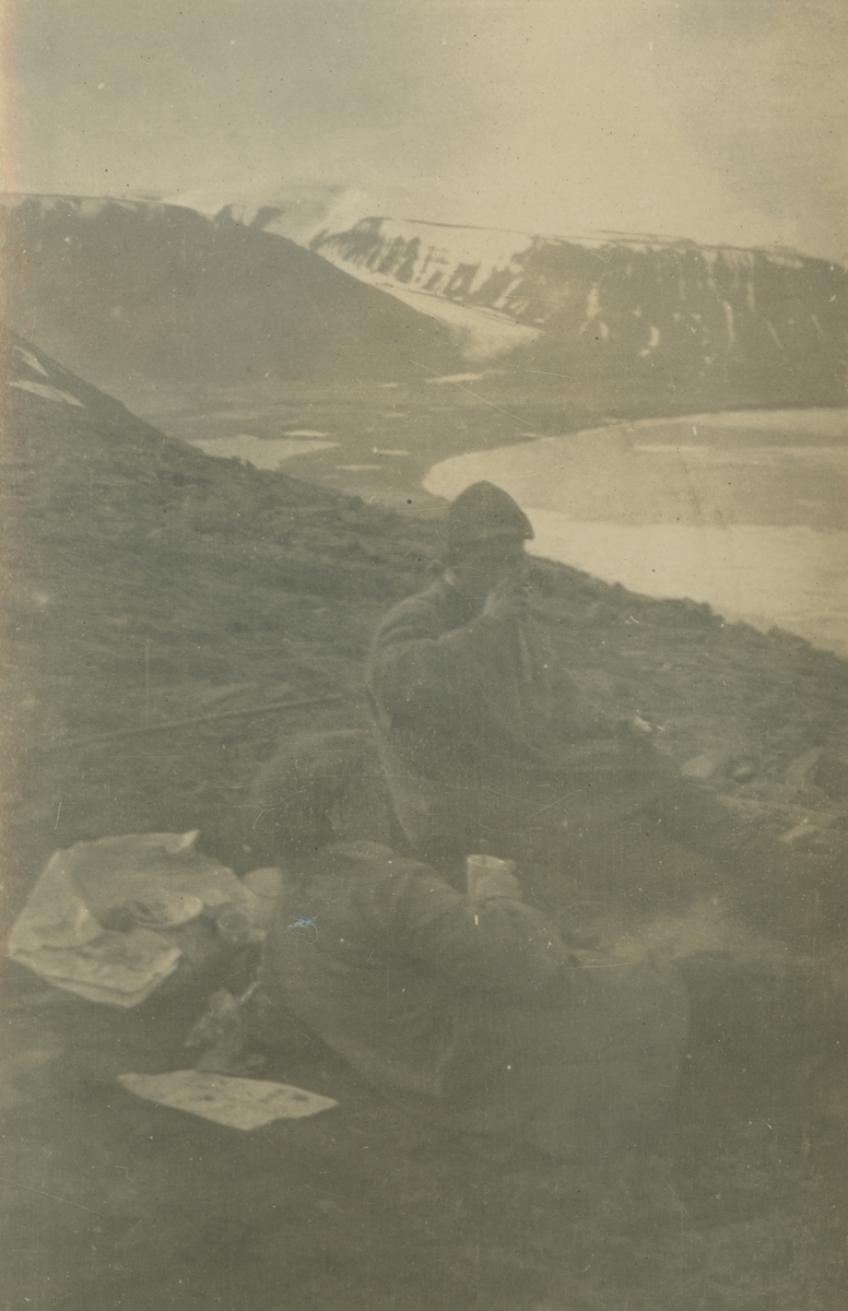 Fotografi från expedition till Spetsbergen. Motiv av expeditionsdeltagare som vilar och fikar på stenig strand i bergslandskap.