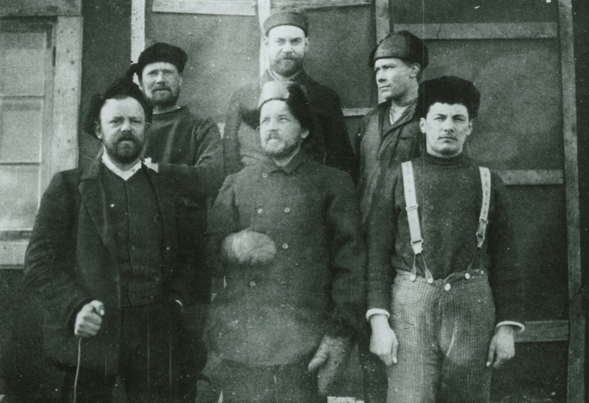 Fotografi från den första svenska Antarktisexpeditionen 1901-1904. Motiv av Otto Nordenskjöld och flera andra expeditionsdeltagare som står framför huset i Snow Hill. Männen i främre raden är Gösta Bodman, Otto Nordenskjöld och Sobral. I bakre raden: Jonasson, Ekelöf och Åkerlund.