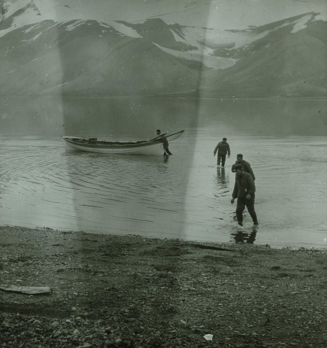 Fotografi från expedition till Spetsbergen. Motiv av fyra män med båt vid strand.