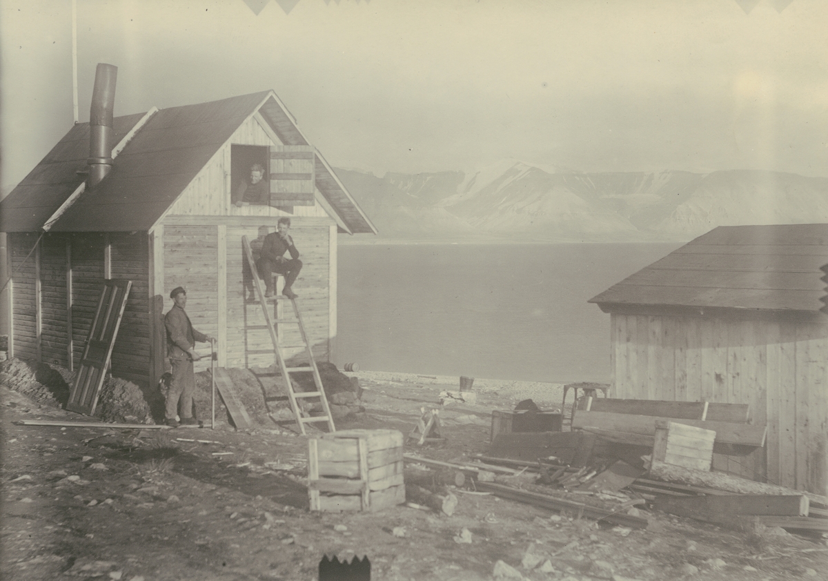 Fotografi från expedition till Spetsbergen 1920. Motiv av tre män och trähus.