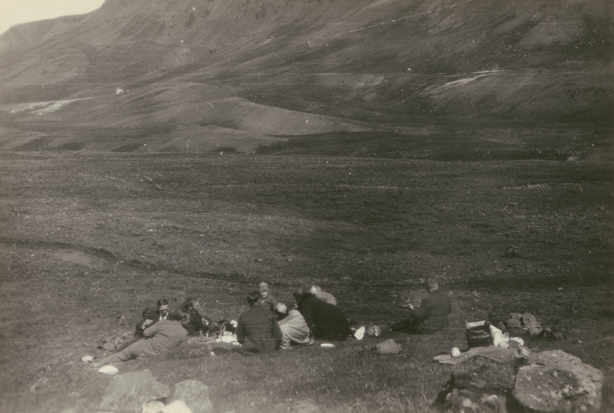 Fotografi från Albin Ahrenbergs resa till Grönland 1929. Motiv av en grupp människor som sitter och vilar i ett kargt bergslandskap. Troligen Island.