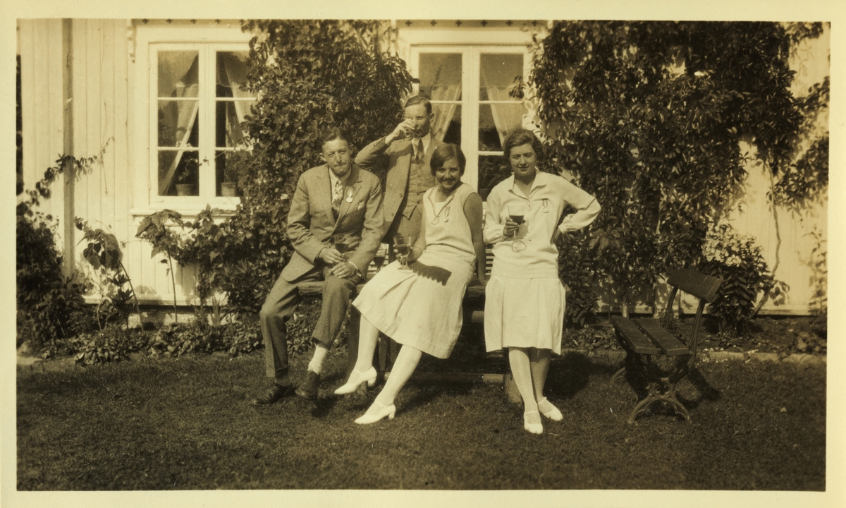 To menn og to kvinner, alle medlemmer av "Kulinarisk klub", sittende på bord utenfor bolighus. Kvinnene er fra venstre Sisken Skjelderup og Cecilie Broch. Antagelig fotografert sommeren 1926.