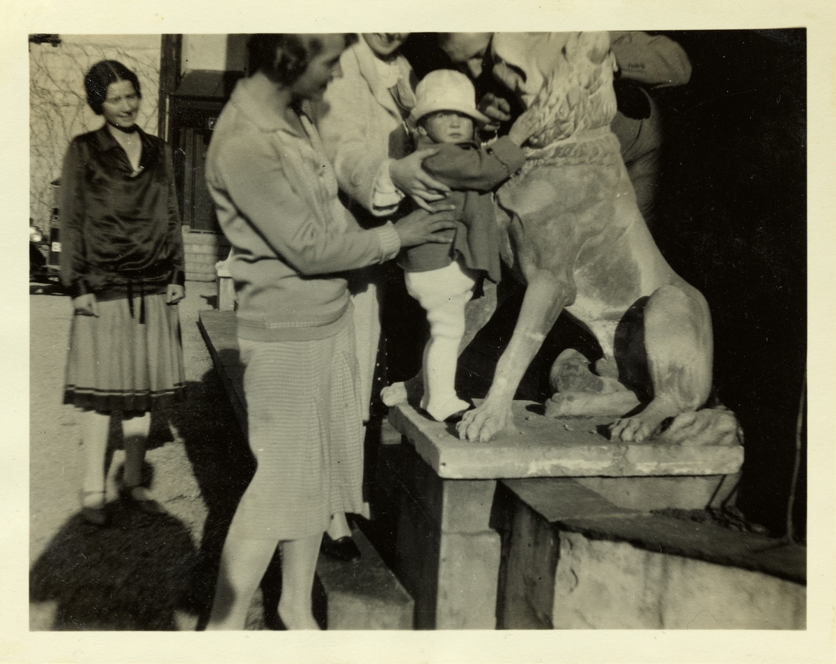En liten jente får klappe en ulveskulptur ved inngangen til eiendommen Lagåsen i Bærum. Til venstre antagelig Lucy Egeberg. Fotografert juni 1928.