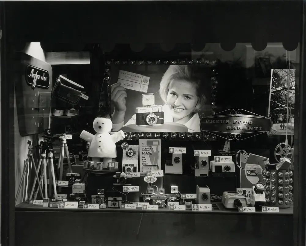 Shop window with cameras for sale and a photograph of a smiling woman. Black and white photograph.