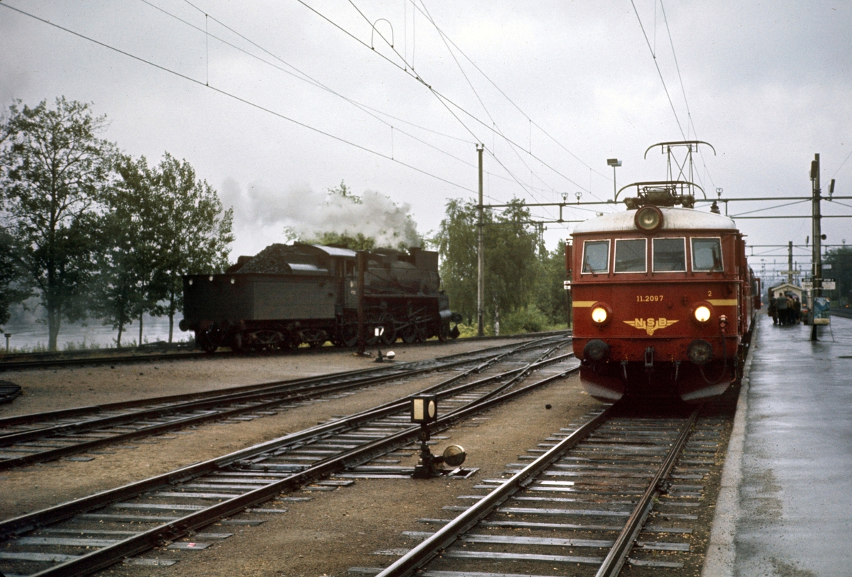Damplokomotiv type 26c nr. 433 på Kongsvinger stasjon. Elektrisk lokomotiv El 11 2097 med persontog til Oslo Ø til høyre