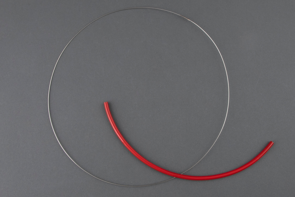 Halssmykke bestående av en tynn stålring der det er tredd på en halvsirkelformet, rødlakkert messingstav.